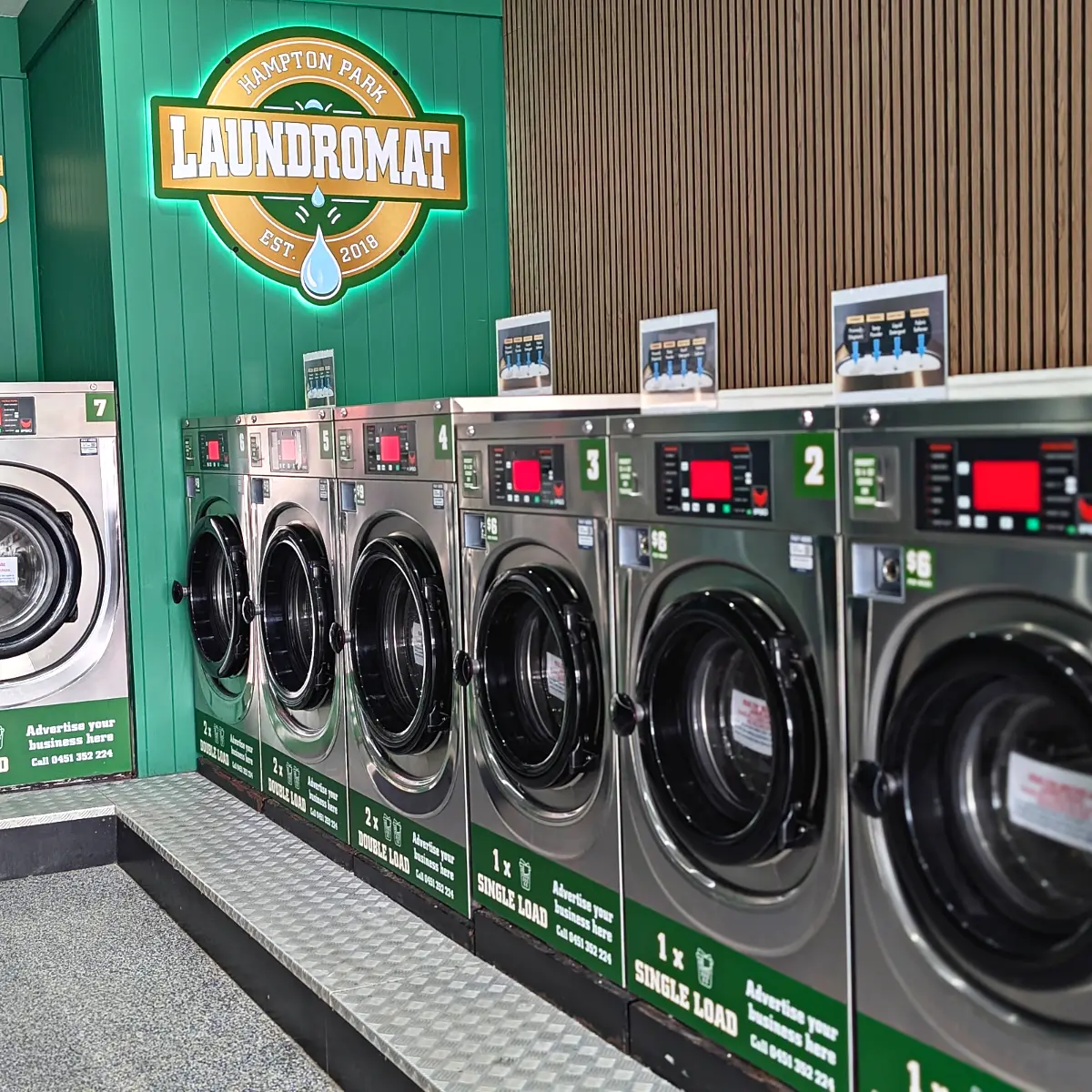 A row of washers under the lit Hampton Park Laundromat sign